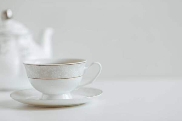 White cup of tea on a white saucer and teapot, background