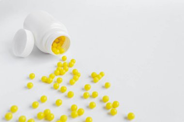 Beyaz arka planda beyaz bir kavanozdan beyaz bir masaya saçılmış yuvarlak sarı vitaminler.