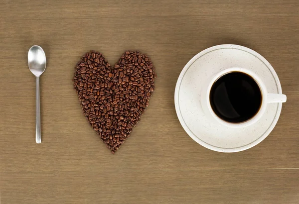 I love coffee. Heart shape made from coffee beans with a spoon and cup of coffee on hessian spelling