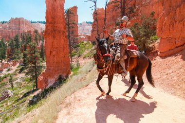 BRYCE CANYON, UTAH - June 27, 207: People riding on horses on the hiking trails in Bryce Canyon National Park on September 3, 2015. Horse riding tour are popular by tourist in the Bryce Canyon. clipart