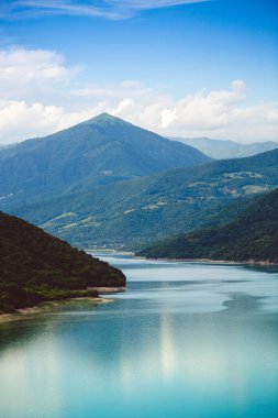 Gürcistan 'daki güzel dağ gölü, Zhinvali rezervuarı. Turkuaz renkli suları Kafkas dağları ile çevrilidir. Güneşli bir günde mavi gökyüzü ve bulutlarla nefes kesici bir manzara..