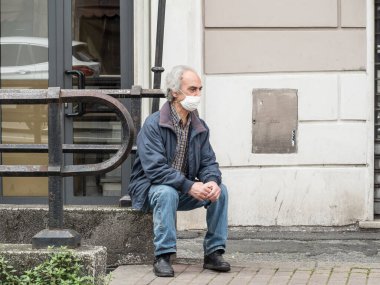 Cenova, otobüs durağında bekliyor. Maske takıyor ve COVID 19 virüsü taşıyor.
