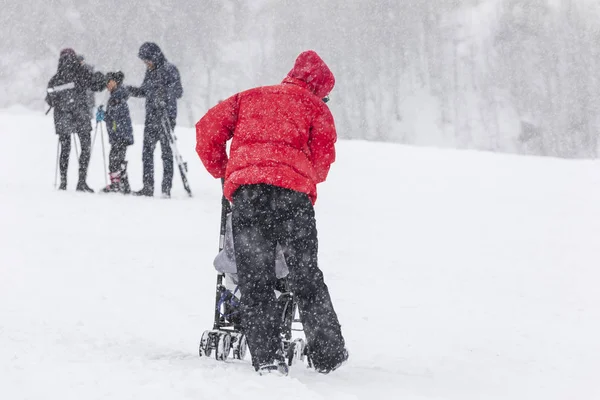 Muž jezdí na dítěti v kočárku na sněhu na sjezdovce — Stock fotografie