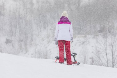 Genç kız inişten kaymaya hazırlanıyor.