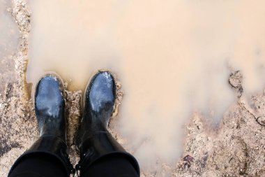 Sulu kahverengi çamurda duran siyah uzun botlar..