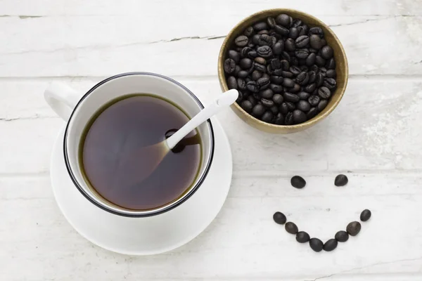 Black coffee in white cup and coffee beans with spoon and smilin