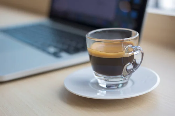 Un vaso de café y un portátil sobre la mesa . — Foto de Stock