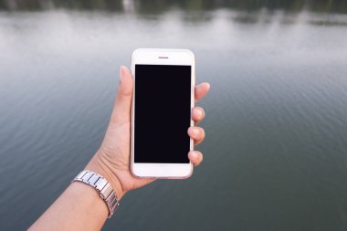 akıllı telefon nehir arka planda tutan kadın el.