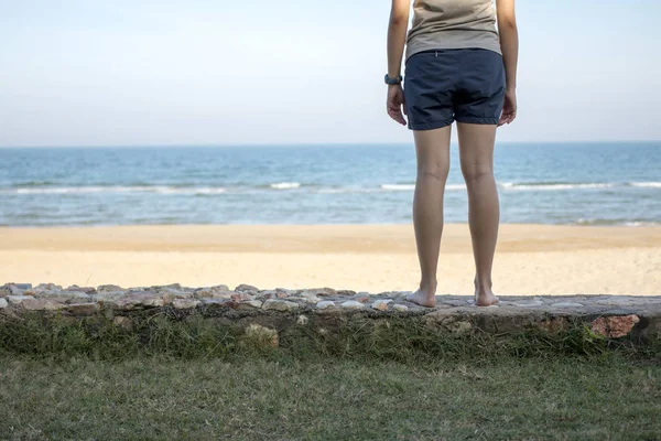 Young woman standing alone and looking at the sea.