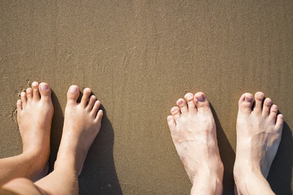 Man och kvinna fötter stående på brun sandstrand. — Stockfoto