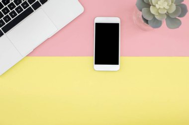 Akıllı telefon, laptop ve etli pastel sarı ve pembe arka plan üzerinde düz lay.