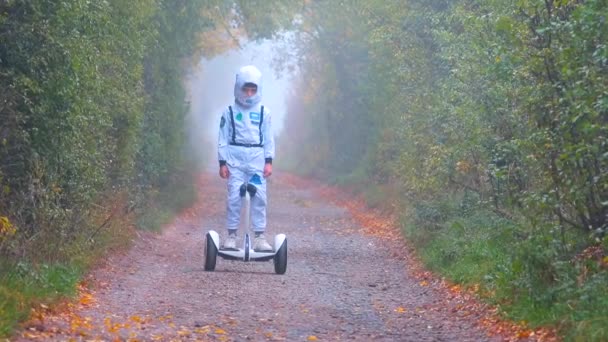 Un niño con un traje blanco se mueve en un giroscooter a lo largo de la carretera brumosa . — Vídeos de Stock