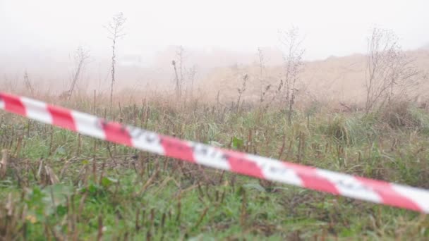 Misdaadplek in een mistig veld. Rood-witte tape omsluit de plaats van plakken. — Stockvideo