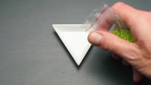 Zöld gyöngyök öntése egy háromszög alakú lemezbe — Stock videók