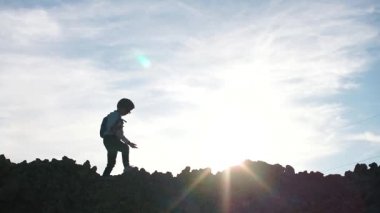 Tepede yürüyen bir çocuğun silueti. Gökyüzüne karşı.
