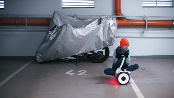 Een jongen zittend op een gyroscooter rijdend rond de ondergrondse parkeerplaats. — Stockvideo