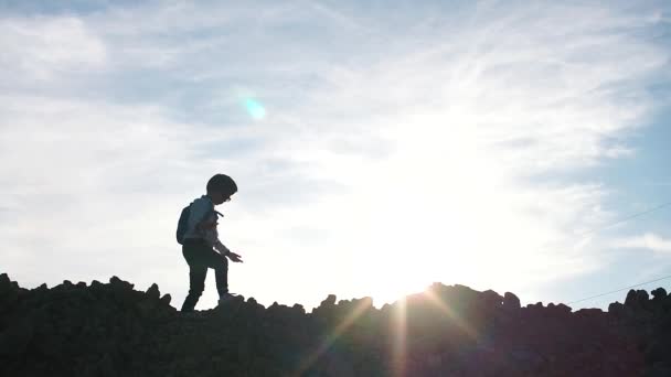 Silhouette eines Jungen, der auf einem Hügel geht. gegen den Himmel. — Stockvideo