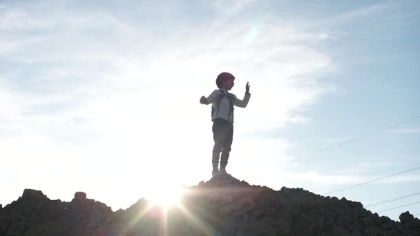 Silhueta de um menino turístico fica na montanha contra o pano de fundo do sol . — Vídeo de Stock