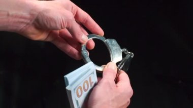 Elleri yakın çekim. Kelepçelerin ve bir deste doların ellerinde..