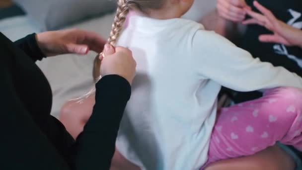 Крупним планом зав'язують коси на голову дочкам. Поруч знаходяться дві лесбіянки . — стокове відео