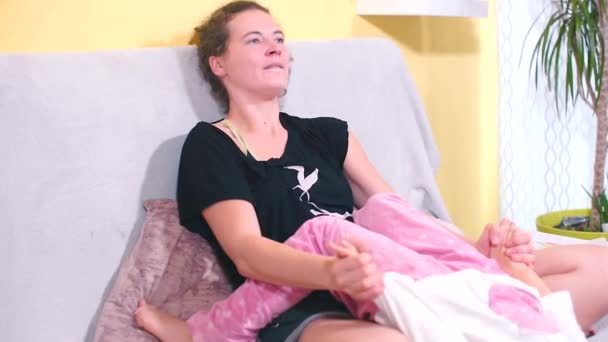 Máma a dcera sedí na gauči. Dítě leží na klíně své matky. — Stock video