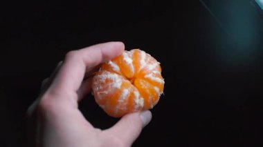 Mandalina kabuğu soyulmuş, elleri siyah bir arka planda.