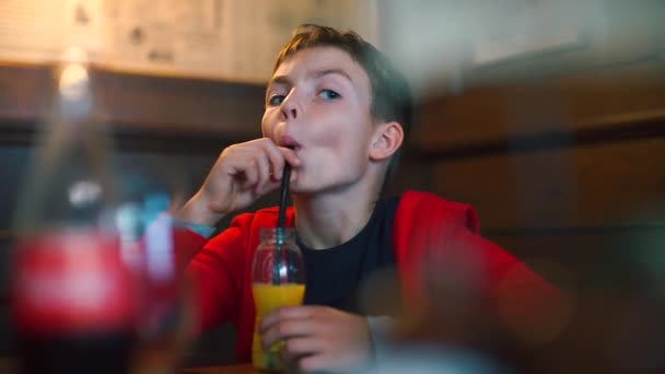 Niño en un restaurante de la escuela bebe jugo de una botella a través de una paja — Vídeos de Stock