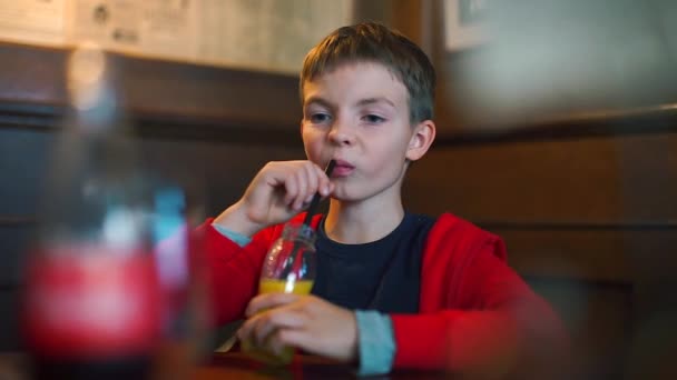 坐在桌旁的小孩的特写镜头，喝着瓶子里的果汁 — 图库视频影像