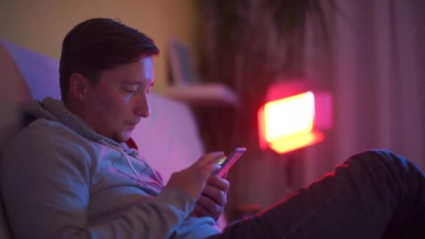 Een man gebruikt 's avonds een smartphone thuis — Stockvideo