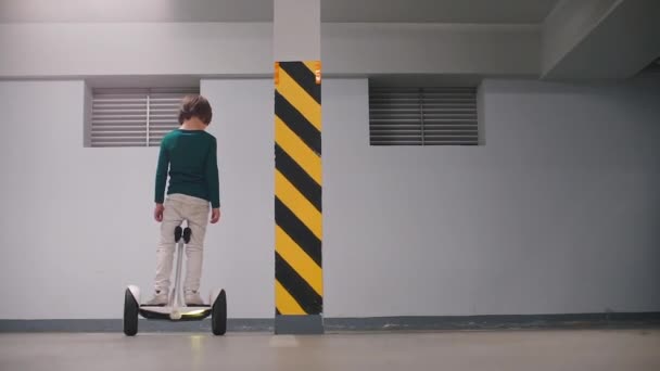 El niño aprende a montar un giroscooter en un aparcamiento subterráneo . — Vídeos de Stock