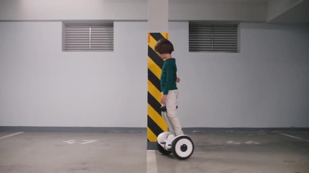 O menino monta um giroscópio em um estacionamento subterrâneo na garagem . — Vídeo de Stock