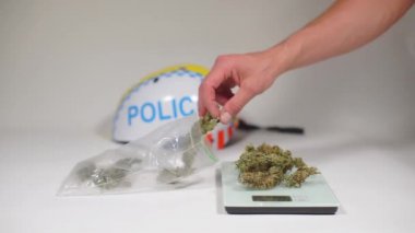 El, yazıt polisinin karşısındaki teraziye esrar koyar.