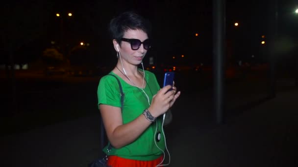 眼鏡をかけた少女は夜にスマートフォンで自撮りをします — ストック動画