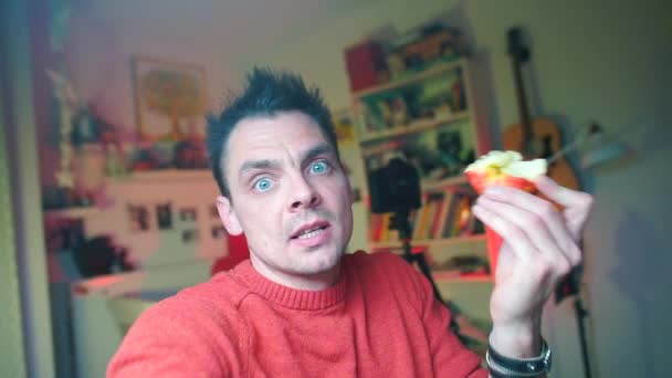 Un blogueur en vêtements rouges tient une caméra dans ses mains et mange une pomme . — Video