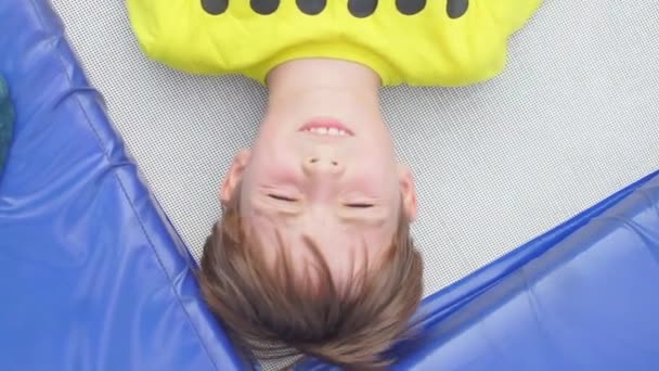 The boy lies on a trampoline and looks up — ストック動画