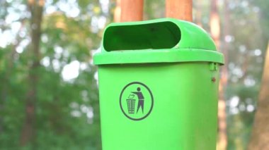 Adam ormandaki çöpe plastik bir şişe atıyor.