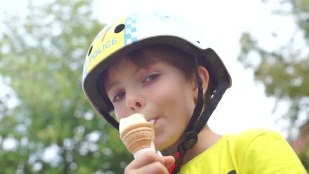 Schoolboy in a helmet eats ice cream, looking at the camera — Stock Video