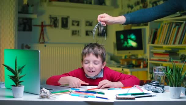 Un garçon est assis à une table à l'école. Une main lui donne un massage de la tête . — Video