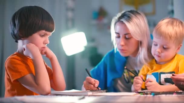 Deux garçons avec un professeur dessinent sur papier sur une table dans un jardin d'enfants . — Video