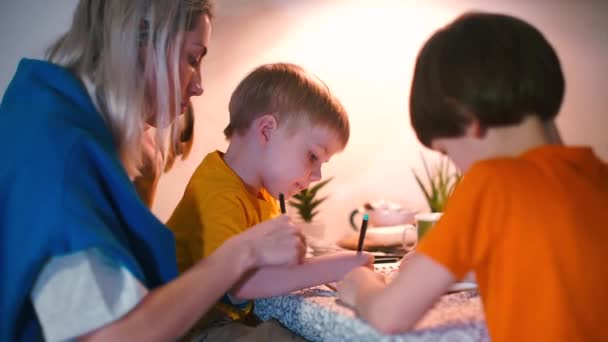 A young mother with two children at the table does school assignments. — Stock Video