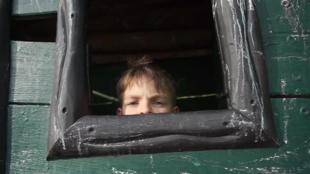 Niño mira por la ventana de una casa de madera para niños — Vídeos de Stock