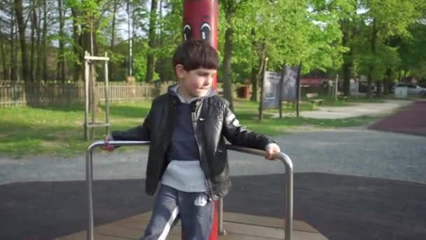 En pojke leker, snurrar på en tur på en lekplats — Stockvideo