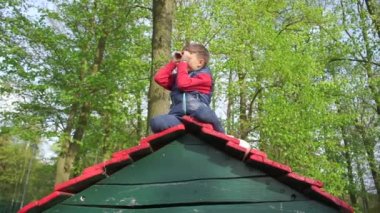 Çocuk evin çatısında oturuyor, teleskopta bakar gibi ellerine bakıyor.