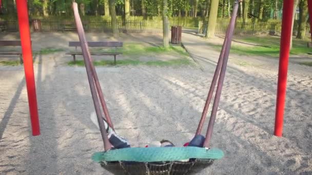 Two children ride on a swing at the school site — ストック動画