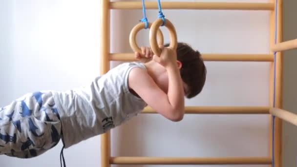 El niño hace flexiones en los anillos deportivos, la pared sueca — Vídeo de stock