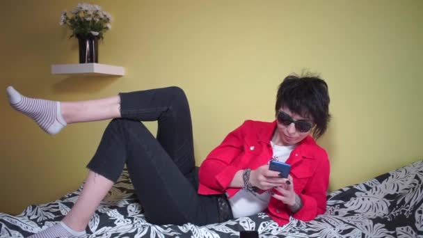 Chica utiliza el Internet en el teléfono mientras está acostado en el sofá — Vídeos de Stock