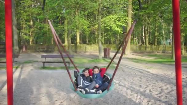 Játszótér a városban, gyerekek fekszenek a hintán a parkban — Stock videók