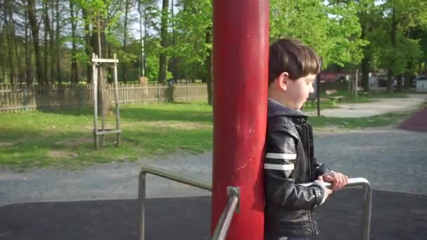 Menino girando em um carrossel no playground na escola — Vídeo de Stock