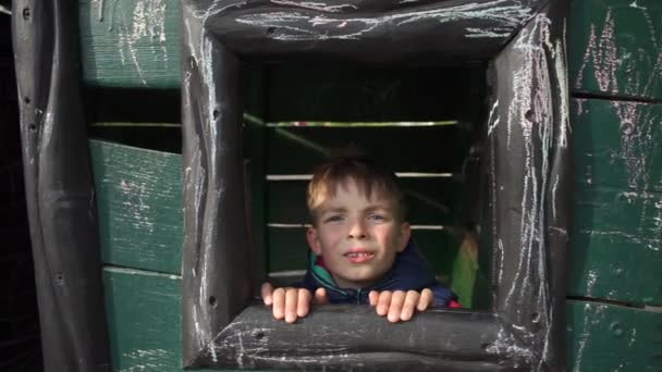 O menino olha para fora de uma janela de madeira, caretas — Vídeo de Stock