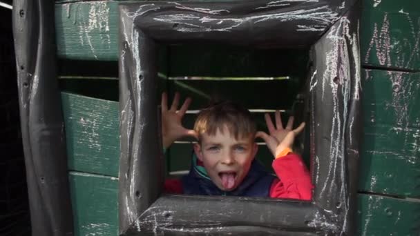 En tonåring leker i ett trähus, tittar ut genom fönstret, grimaser — Stockvideo